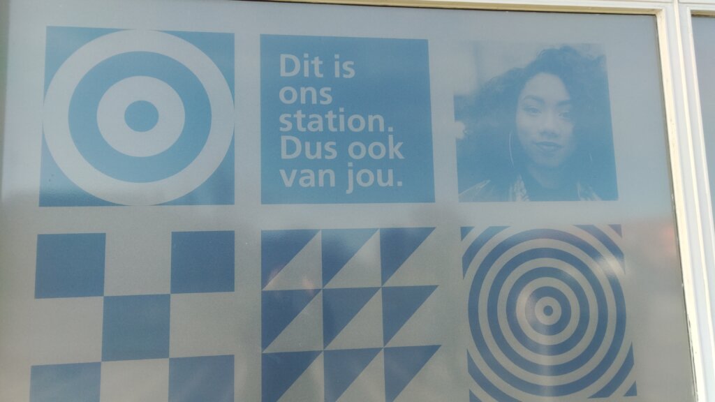 Poster in a grid with symbols, a black girl with curly hair, next to a text block in Dutch "Dit is ons station. Dus ook van jou."